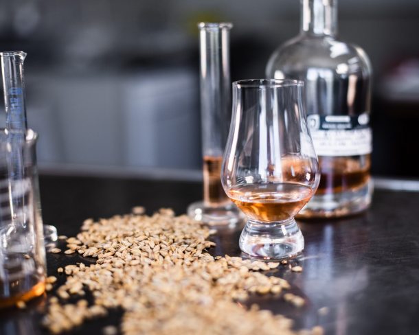 A bottle of whisky with a small glass, and a pile of malts spread out on the table