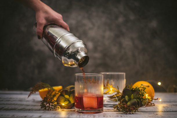 A hand pours a shaker into a whisky glass surrounded by garnishes, ingredients and candles - best Japanese whisky for cocktails