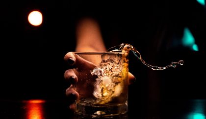A hand cheersing a whisky glass while spilling some over top