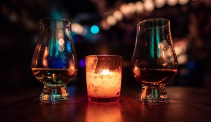 Two whisky glasses in a dark-lit bar with a candle between them.